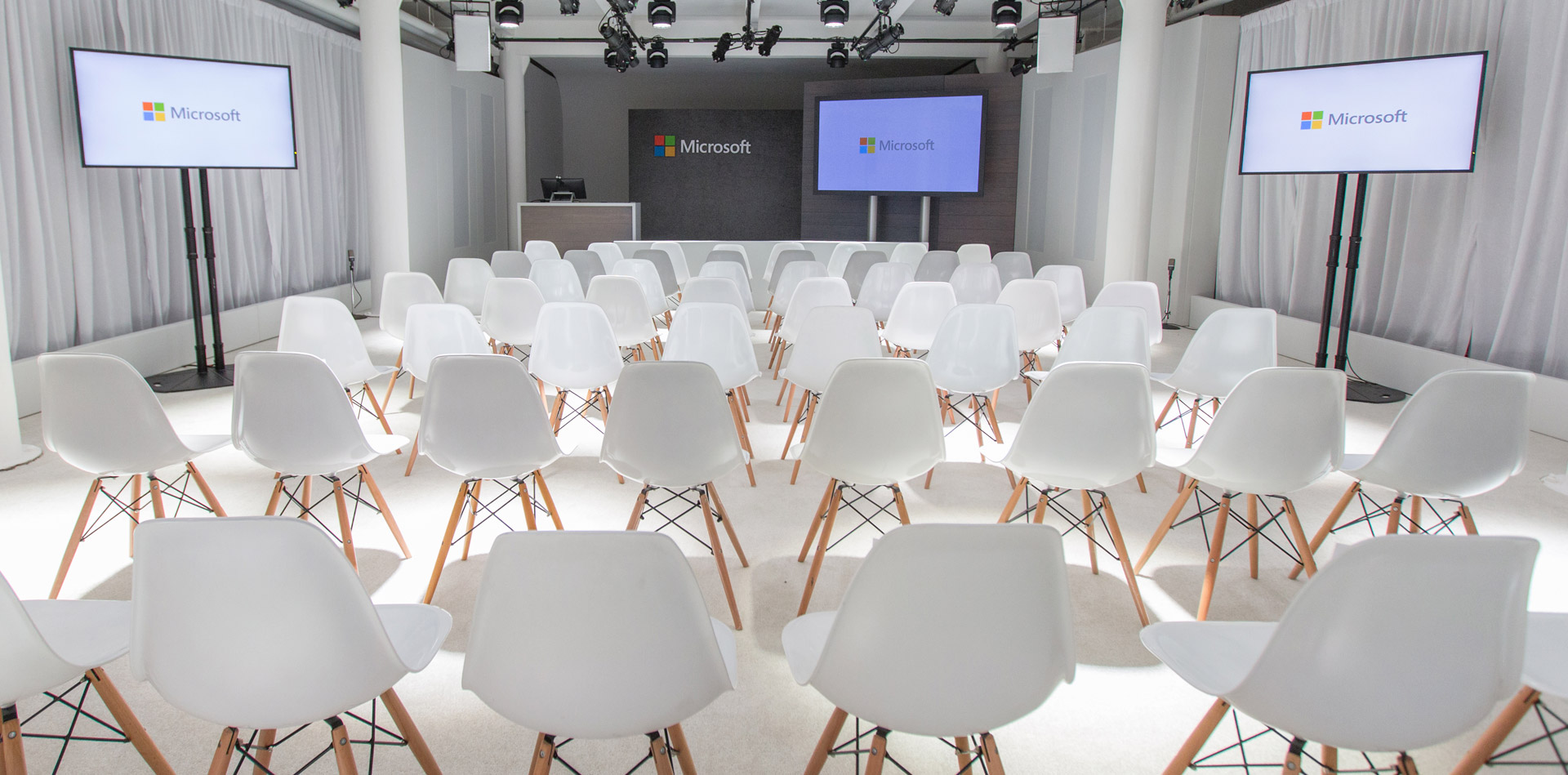 Conference room with white chairs and multiple screens with the Microsoft brand.