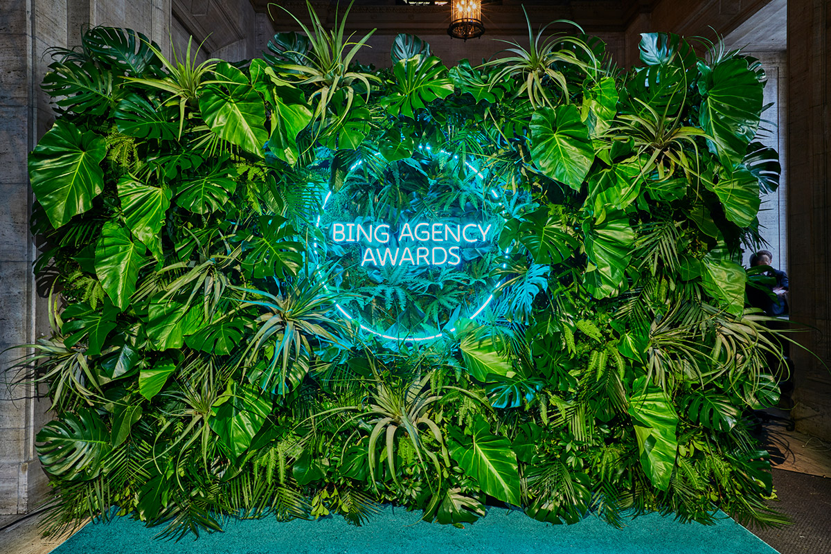 Decorative wall of green plants with neon blue sign in the middle that says Bing Agency Awards