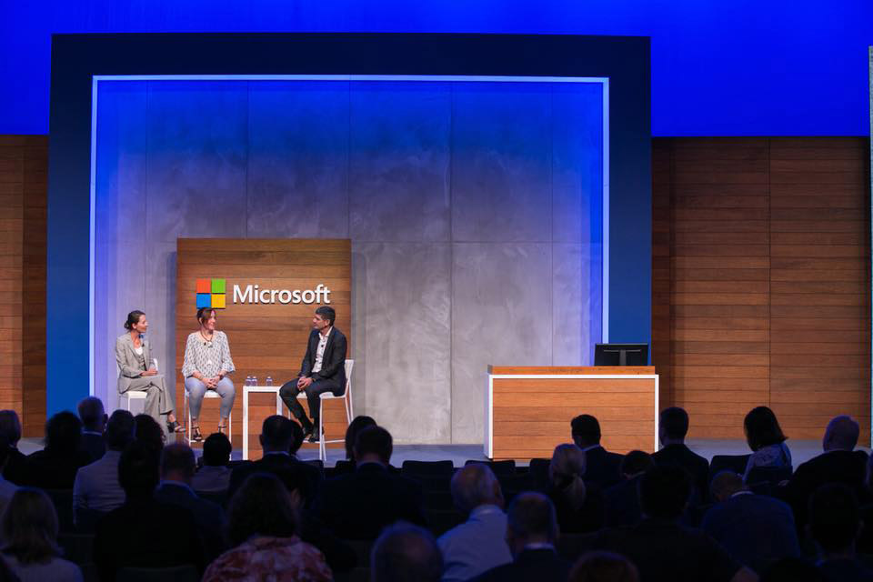 Stage with three people seated in front of a Microsoft branded wall