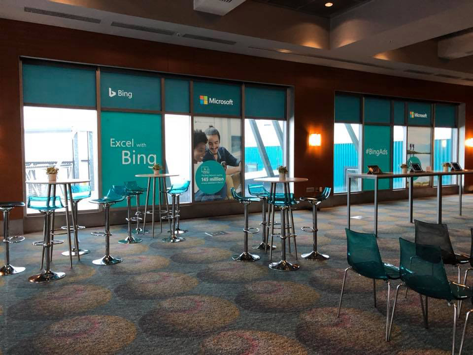Room with cocktail rounds and Bing branding on windows.