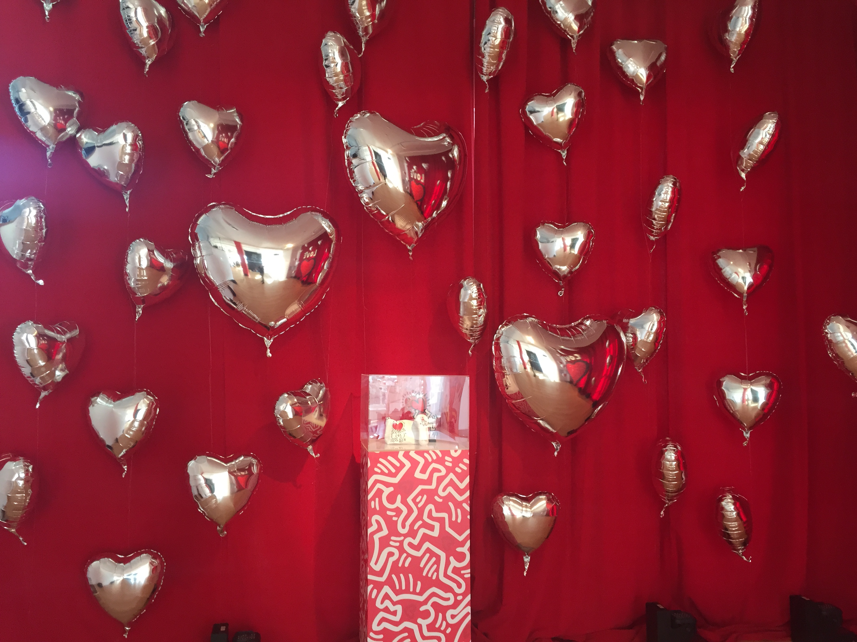 Red backdrop with multiple silver heart-shaped balloons.