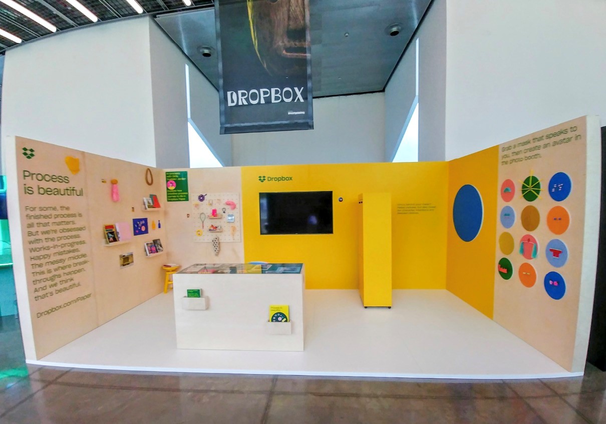 Dropbox trade booth with yellow backdrop and infographics.